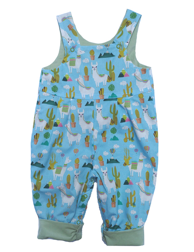 Llama Reversible Dungarees by Seesaw, llama print side shown, sky blue with white llamas, cacti and colourful saddle blankets, cuffed hems